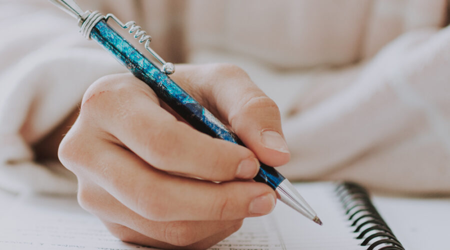 A vertical selective closeup of a female writing in a notebook with a blue pen